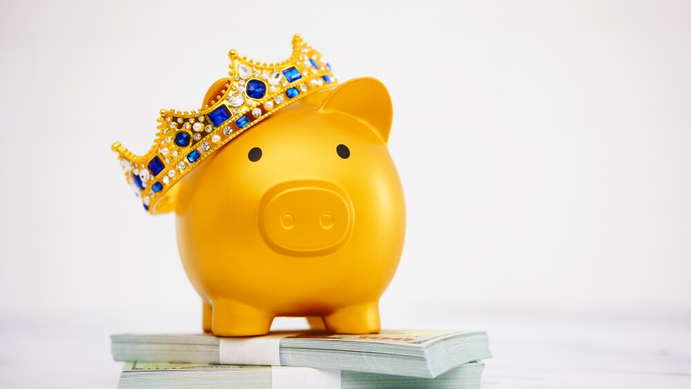 Gold piggy bank wearing crown standing on a stack of American currency dividend aristocrat royalty