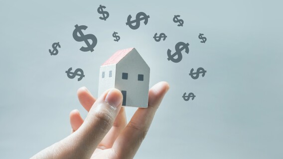 A hand holding a wooden home with dollar signs showing how you can profit from real estate right now