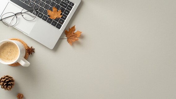 Autumn-inspired office theme. Top view of laptop, steaming mug of pumpkin spice latte, stylish spectacles, golden maple leaves, pine cones, star anise on grey backdrop with empty space for text or ad